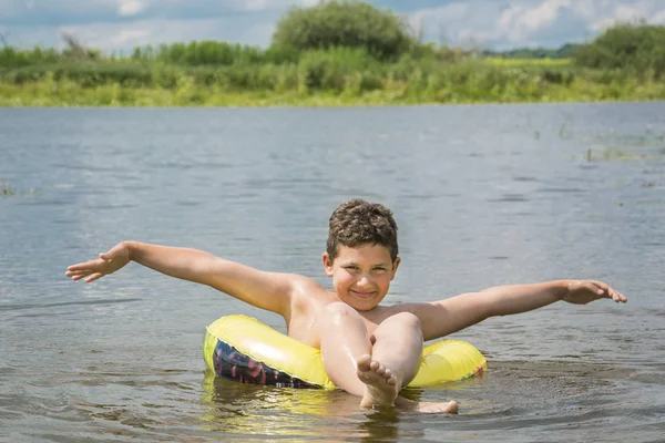 En verano, en un día brillante y soleado, un niño nada a lo largo del río en un círculo inflable . —  Fotos de Stock