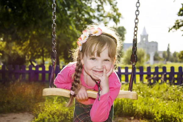 En el verano en el parque una pequeña chica divertida está montando en un swi —  Fotos de Stock