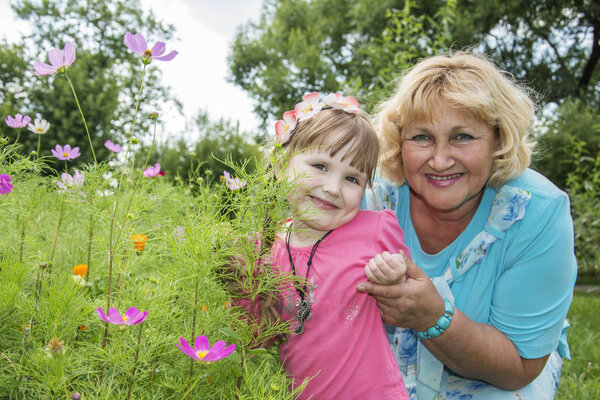 In summer, in a bright sunny day in the park, the grandmother and granddaughter play near the flowers.