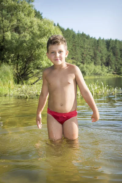 夏天, 在炎热的日子里, 一个男孩穿着红色的泳衣站在水中 — 图库照片