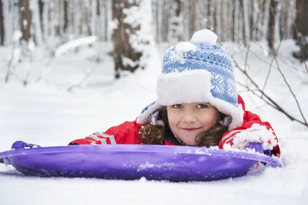 In inverno, nel bosco nella neve giace una piccola ragazza riccia . — Foto Stock