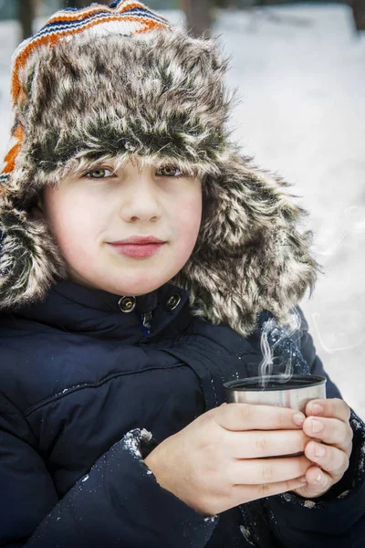 En invierno, el niño bebe té caliente en el bosque. . — Foto de Stock