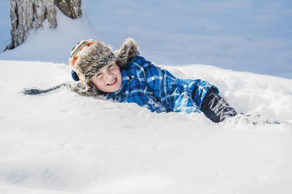 På vintern ligger en glad pojke på snön. — Stockfoto