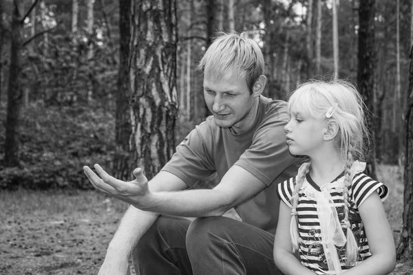 In the summer, the father and daughter are sitting in the forest