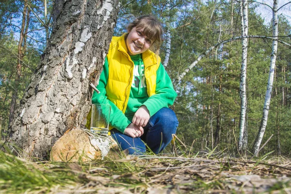 春の白樺林では 明るい晴れた日に 女の子はガラス容器に白樺の樹液を収集します — ストック写真