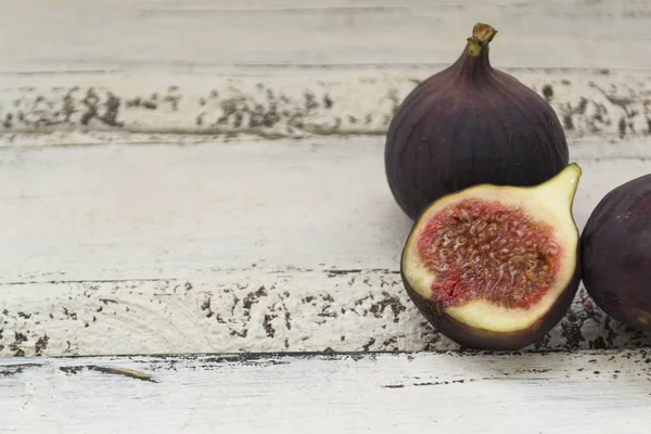 Three fresh figs on a wooden white table. One fig is cut in halves and its flesh is visible. Located in a group. — Stock Photo, Image