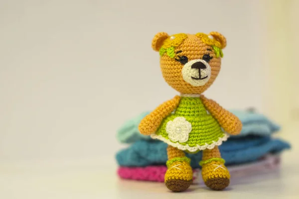 Knitted toy yellow bear in knitted colored clothes - colored amigurumi toy on a light background. Copy space. Hobby concept.