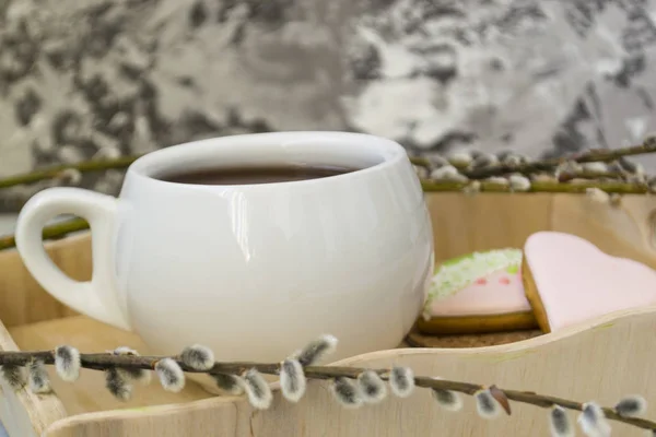 Una ramita de sauce con brotes y una taza de té blanco se encuentra en una bandeja de madera. El concepto de mañana, desayuno —  Fotos de Stock