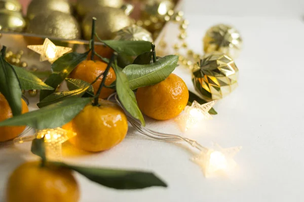 Orange mandarin on the background of blurry mandarin and golden balls. Frosty winter composition on a silver bokeh background with glitter garlands. Orange citrus fruits and leaves macro shot. There is a place for text.