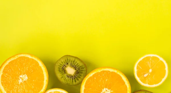 Fruit frame. Colorful fresh citrus fruits on a light green background. Orange, tangerine, lemon and kiwi are cut in half. Flat lay, top view, copy space. Healthy eating concept.