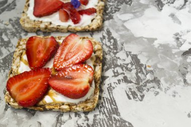 Beton bir masada tereyağı, reçel, çilek ve muzla tereyağlı tost makinesi ve yulaf ekmeği ile kahvaltı. Faydalı yaz yemekleri konsepti.