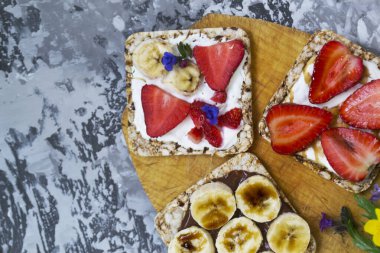 Beton bir masada tereyağı, reçel, çilek ve muzla tereyağlı tost makinesi ve yulaf ekmeği ile kahvaltı. Faydalı yaz yemekleri konsepti.