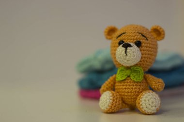 Beyaz arka planda oturan yeşil kurdeleli turuncu ayı Amigurumi. İğne işi konsepti. Metin için bir yer var.