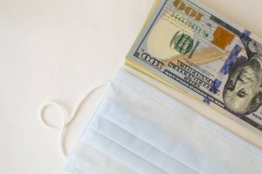 Koruyucu maske ve beyaz arka planda dolar banknotları. Pahalı ilaç kavramı. İlaç endüstrisi ve sağlık sigortası. Metin için bir yer var.
