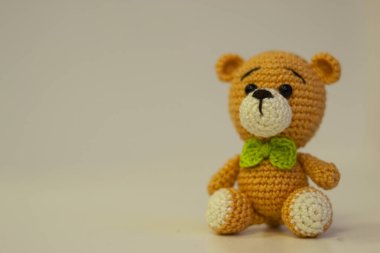 Beyaz arka planda oturan yeşil kurdeleli turuncu ayı Amigurumi. İğne işi konsepti. Metin için bir yer var.