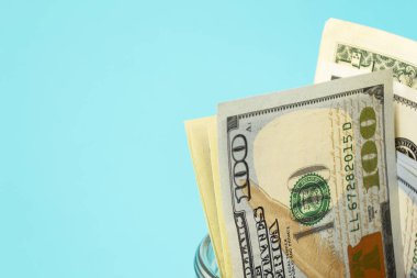 Mavi arka planda, bir litrelik kavanozdaki para. Amerikan doları kumbarada. İş konsepti, finans. Metin için bir yer var.