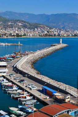 Türkiye 'nin Antalya bölgesindeki Alanya yarımadasında bir marina ve Kyzyl Kule iskelesi bulunan manzara. Mavi Akdeniz, mavi gökyüzü, ufuktaki dağlar ve şehrin evleri. Plaj tatil yeri
