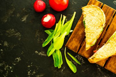 Domatesli ve jambonlu ev yapımı sıcak sandviç. Lezzetli kahvaltıda kızarmış ekmek, kırmızı domates, yeşil salata ve sosis. Yemekler tahtanın üzerinde, ve siyah bir arka planda, düz yatak. Boşluğu kopyala