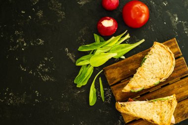 Domatesli ve jambonlu ev yapımı sıcak sandviç. Lezzetli kahvaltıda kızarmış ekmek, kırmızı domates, yeşil salata ve sosis. Yemekler tahtanın üzerinde, ve siyah bir arka planda, düz yatak. Boşluğu kopyala