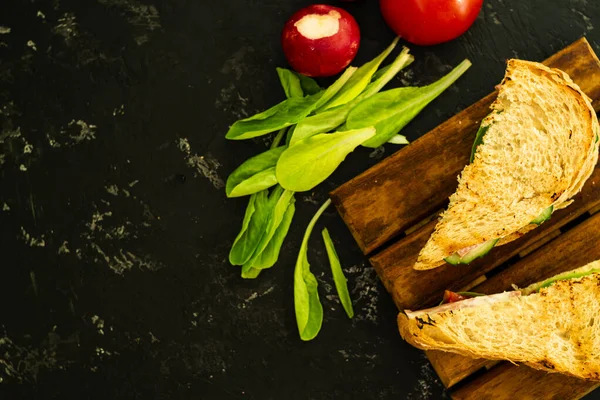 Domatesli ve jambonlu ev yapımı sıcak sandviç. Lezzetli kahvaltıda kızarmış ekmek, kırmızı domates, yeşil salata ve sosis. Yemekler tahtanın üzerinde, ve siyah bir arka planda, düz yatak. Boşluğu kopyala