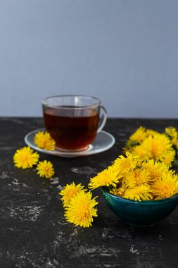 Karahindiba çiçekleri ve siyah bir masada sağlıklı çay. Bulanık arkaplan, kopyalama alanı. Yaz kahvaltısı ve çay