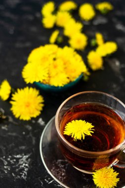 Karahindiba çiçekleri ve siyah bir masada sağlıklı çay. Bulanık arkaplan, kopyalama alanı. Yaz kahvaltısı ve çay