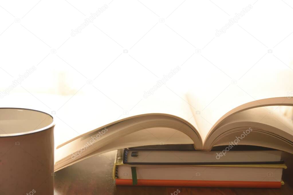 A high key image of book with open pages along with tea cup , book is stacked on various other books