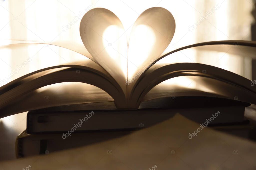 Abstract image of book with open page folded a heart shape , book is stacked on various other books