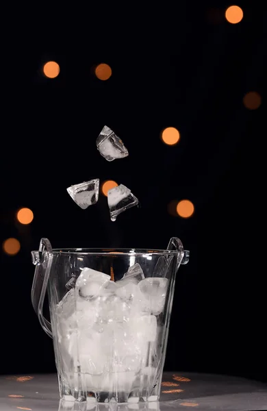 Dropping ice cubes inside ice bucket and photographed against beautiful light bokeh and isolated against black background