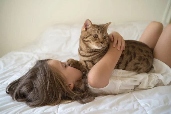 Fiatal lány simogató macska ágyon — Stock Fotó