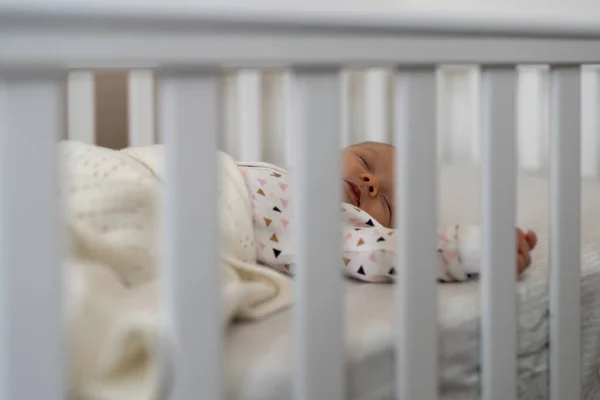 可爱的新生女婴睡在床上 透过婴儿床的栅栏观看 — 图库照片