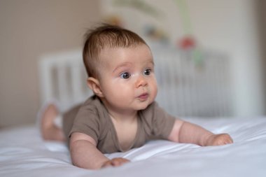 3 aylık bir bebeğin yatakta yatışı ön planda.