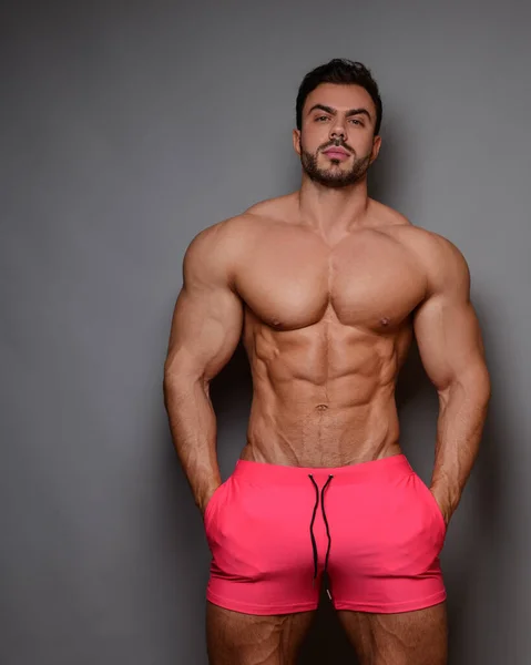 Gri arka planda pembe şortlu üstsüz erkek modelin stüdyo portresi.