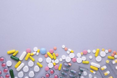 Renkli haplar ve tabletler gri arka planda, üst görünümde.