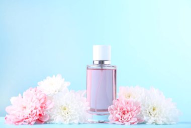 Mavi arka planda beyaz ve pembe çiçekli bir şişe parfüm.