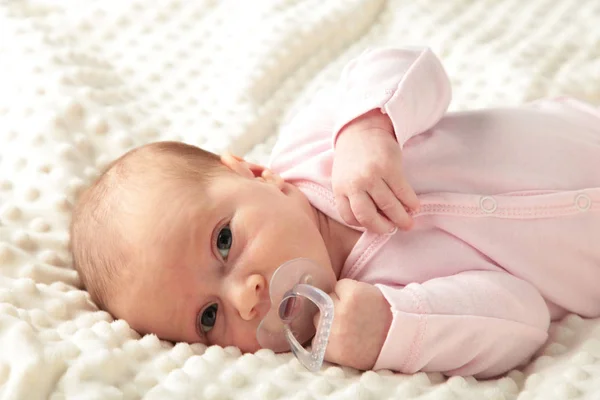 Baby girl lying on white bed and sucks a dummy, top view — Stock Photo, Image