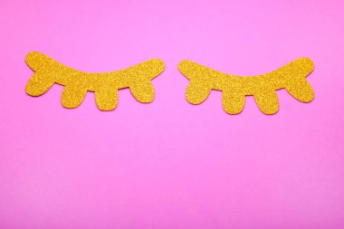 Pembe arka planda altın rengi kirpikler. Üst görünüm