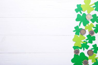 Beyaz ahşap arka planda bozuk paralarla el yapımı kağıt yonca yapraklarından Mutlu Aziz Patrick 'ler.