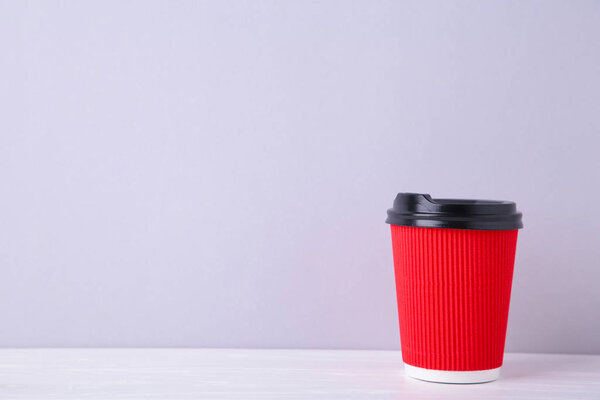 Red paper cup of coffee on grey wooden background