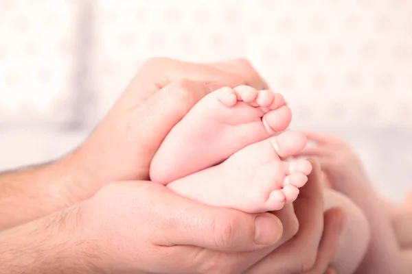 Fader händer håller små babyfötter på sängen — Stockfoto