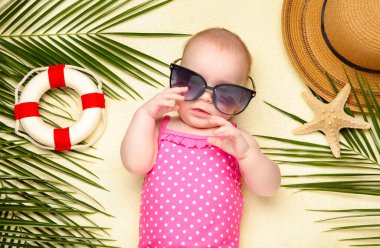 Plaj aksesuarlarıyla güneş gözlüklü bebek. Bebekle deniz tatili, yaz konsepti. Üst görünüm