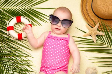 Plaj aksesuarlarıyla güneş gözlüklü bebek. Bebekle deniz tatili, yaz konsepti. Üst görünüm