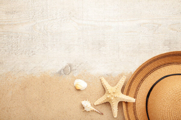 Beach hat with seashells and sand on light background, flat lay
