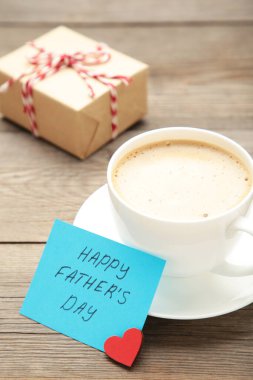 Kahve fincanı ve gri ahşap arka planda hediyeli Babalar Günü mesajı. Üst görünüm