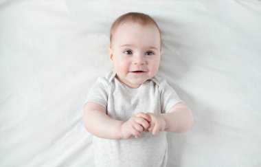 Huzurlu bebek beyaz bir yatakta uzanıyor ve gülümsüyor..