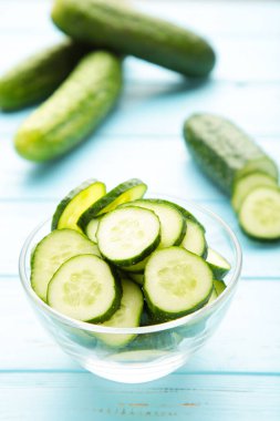 Mavi ahşap arka planda kasede taze salatalık dilimleri. Üst görünüm