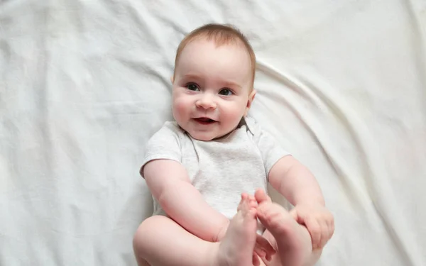 Cute Baby Lying Holding Her Legs White Bed Top View — Stock Photo, Image