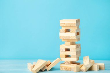 Ahşap Jenga oyununda iş riski kavramı. Mavi arkaplanda tahta bloklar