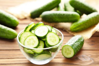 Kahverengi ahşap arka planda, kâsede taze salatalık dilimleri. Üst görünüm