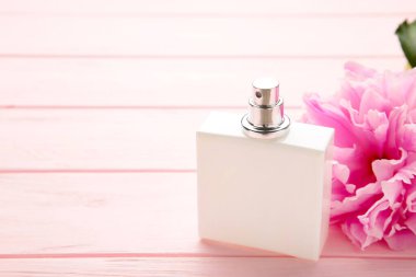 Pembe arka planda pembe çiçekli beyaz bir parfüm şişesi.